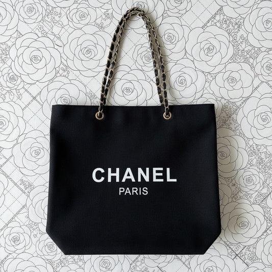 Noticed Atelier by Legzdiamond black canvas Chanel Paris tote with gold chain straps on a white floral background