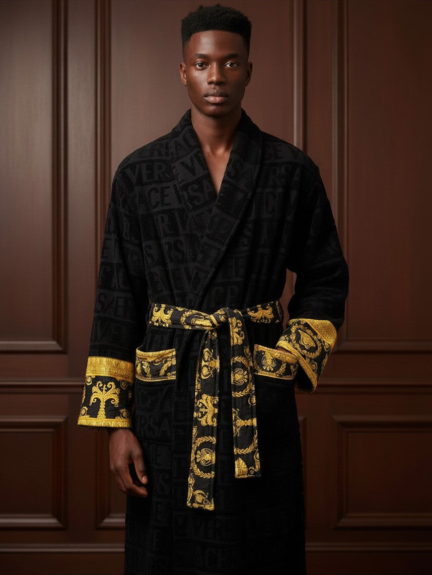 Man wearing a Noticed Atelier by Legzdiamond black plush cotton bathrobe with gold baroque cuffs and waist tie.