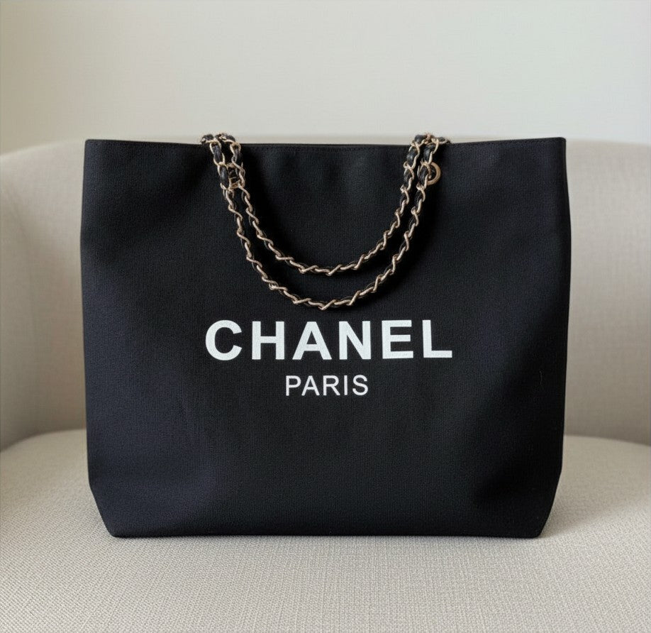 Noticed Atelier by Legzdiamond black canvas Chanel Paris tote bag with gold chain straps on a neutral chair