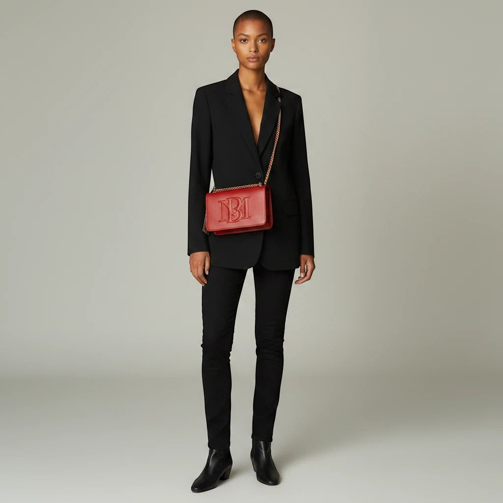 Model wearing a Noticed Atelier by Legzdiamond Badgley Mischka brick red vegan leather crossbody bag with gold chain.