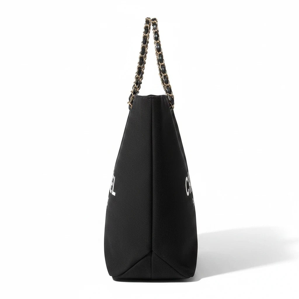 Noticed Atelier by Legzdiamond Chanel tote bag in black with white logo and signature chain strap, side profile view.