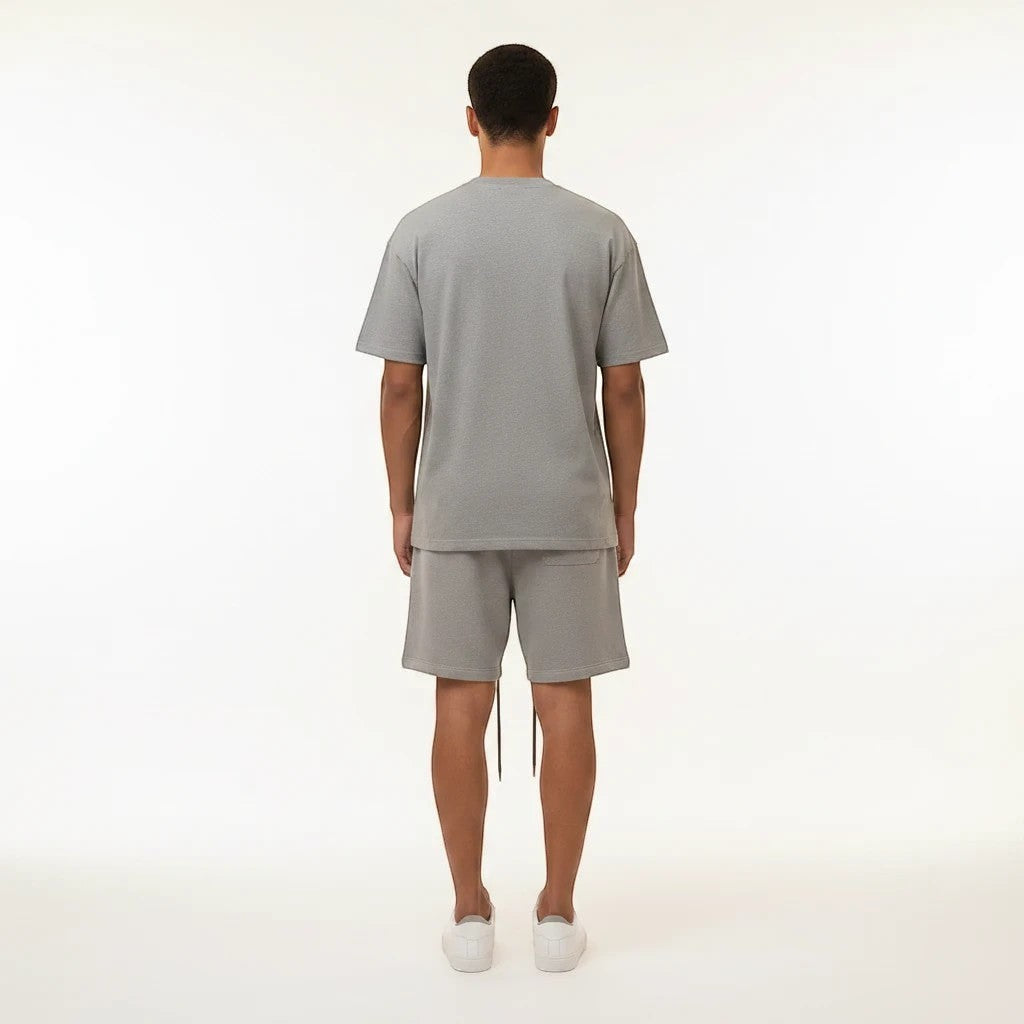 Back view of a man wearing a Noticed Atelier by Legzdiamond heather grey cotton t-shirt and shorts set.