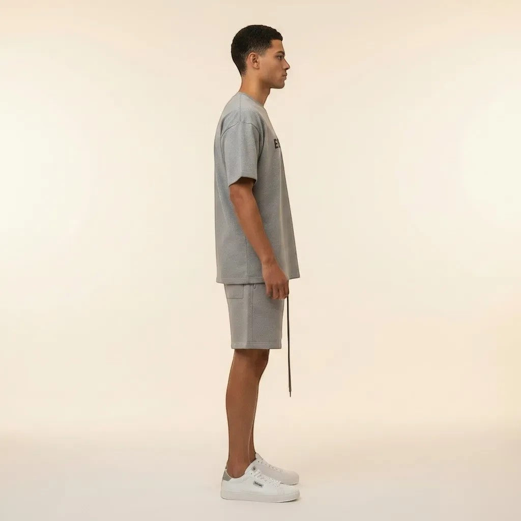 Model wearing a heather grey Essentials Fear Of God cotton t-shirt and shorts set from Noticed Atelier by Legzdiamond